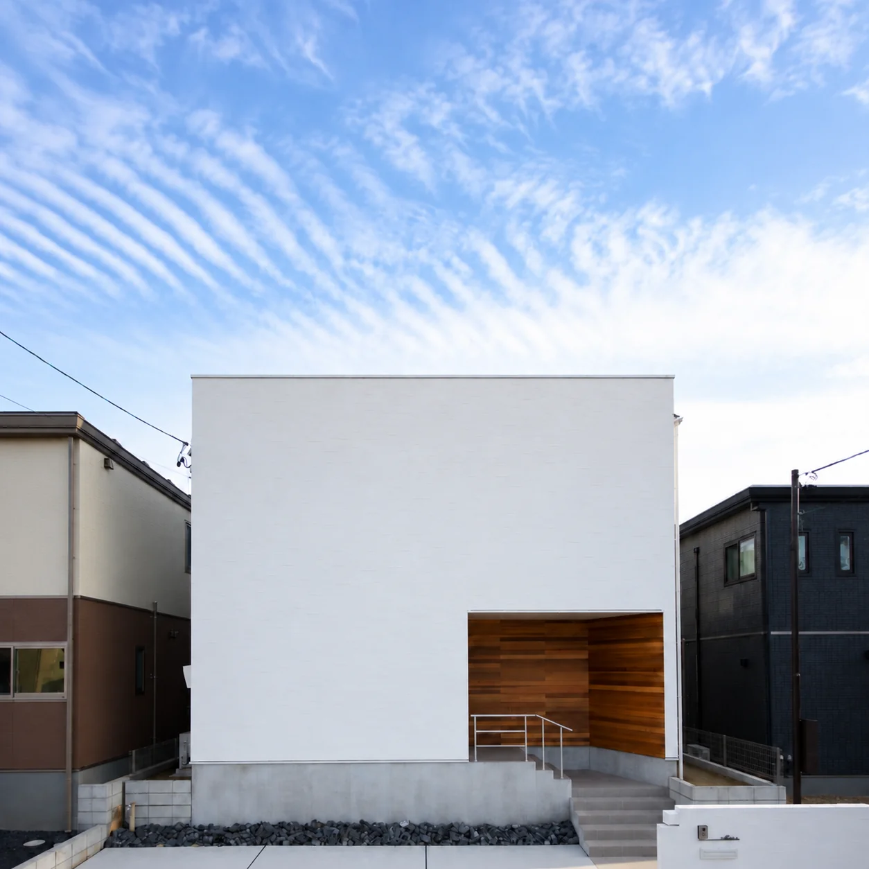 空の下に佇む白い箱型の住まい。木で仕上げた玄関がアクセントになった外観